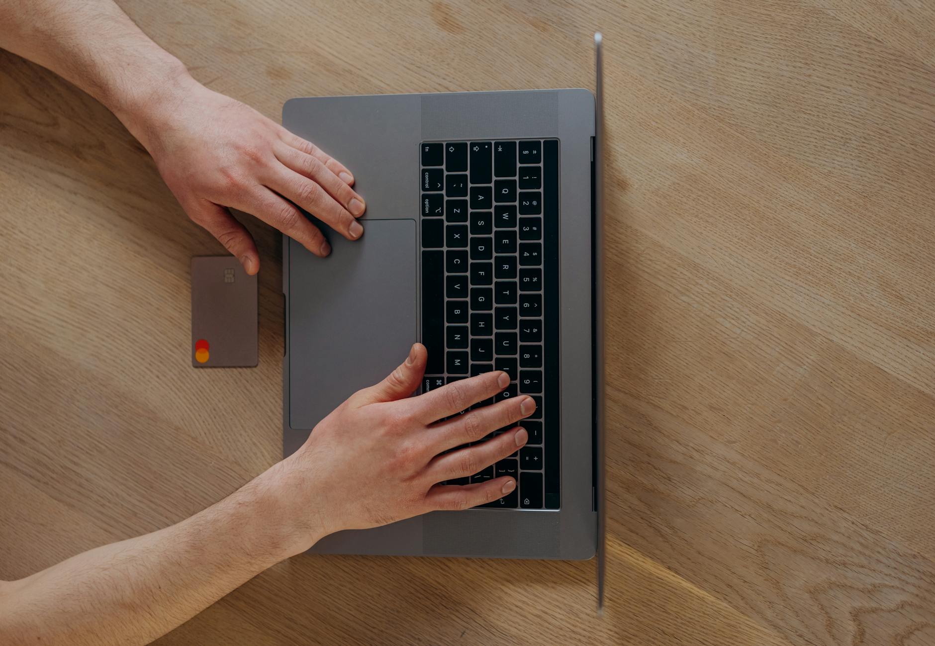 Osoba kupująca laptop online kartą płatniczą przy drewnianym biurku
